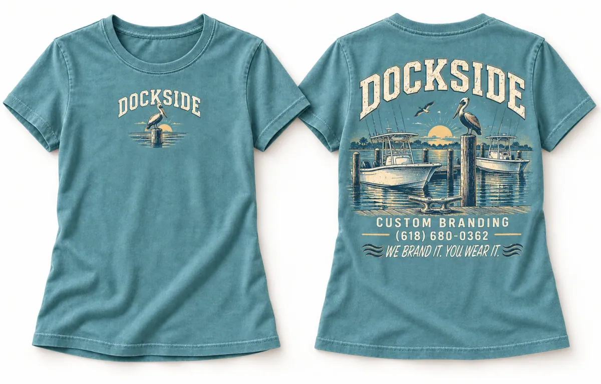 Lagoon blue women's Dockside tee showing a small marina chest print and a large back print with docked boats, pelicans, and a Florida sunset.